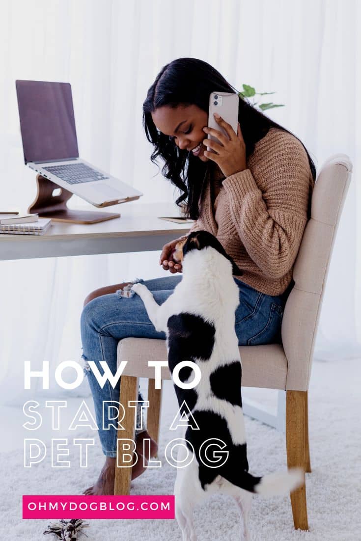 A Black woman wearing rippled blue jeans and a camel-colored sweater sits on a cream-colored fabric desk chair. In front of her on the desk is a pile of notebooks and an open laptop computer. She's talking on her cellphone while petting a small white with black spots dog. The text overlay reads: How to start a pet blog