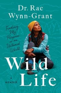 The cover of Wild Life features a picture of Dr. Rae Wynn-Grand, a Black woman wearing a yellow beanie cap, a blue fleece jacket, dark gray hiking pants, and a red backpack, sitting against a dark green background illustrated with line drawings of nature like trees and flowers. She's looking off into the distance.